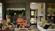 cozy living room with textured walls, large artwork, white sofa with colorful cushions, timber table styled with vase of large stems and coffee table books, rattan armchair, rust linen armchair, side table with silver table lamp