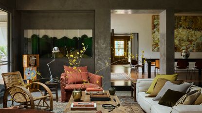 cozy living room with textured walls, large artwork, white sofa with colorful cushions, timber table styled with vase of large stems and coffee table books, rattan armchair, rust linen armchair, side table with silver table lamp