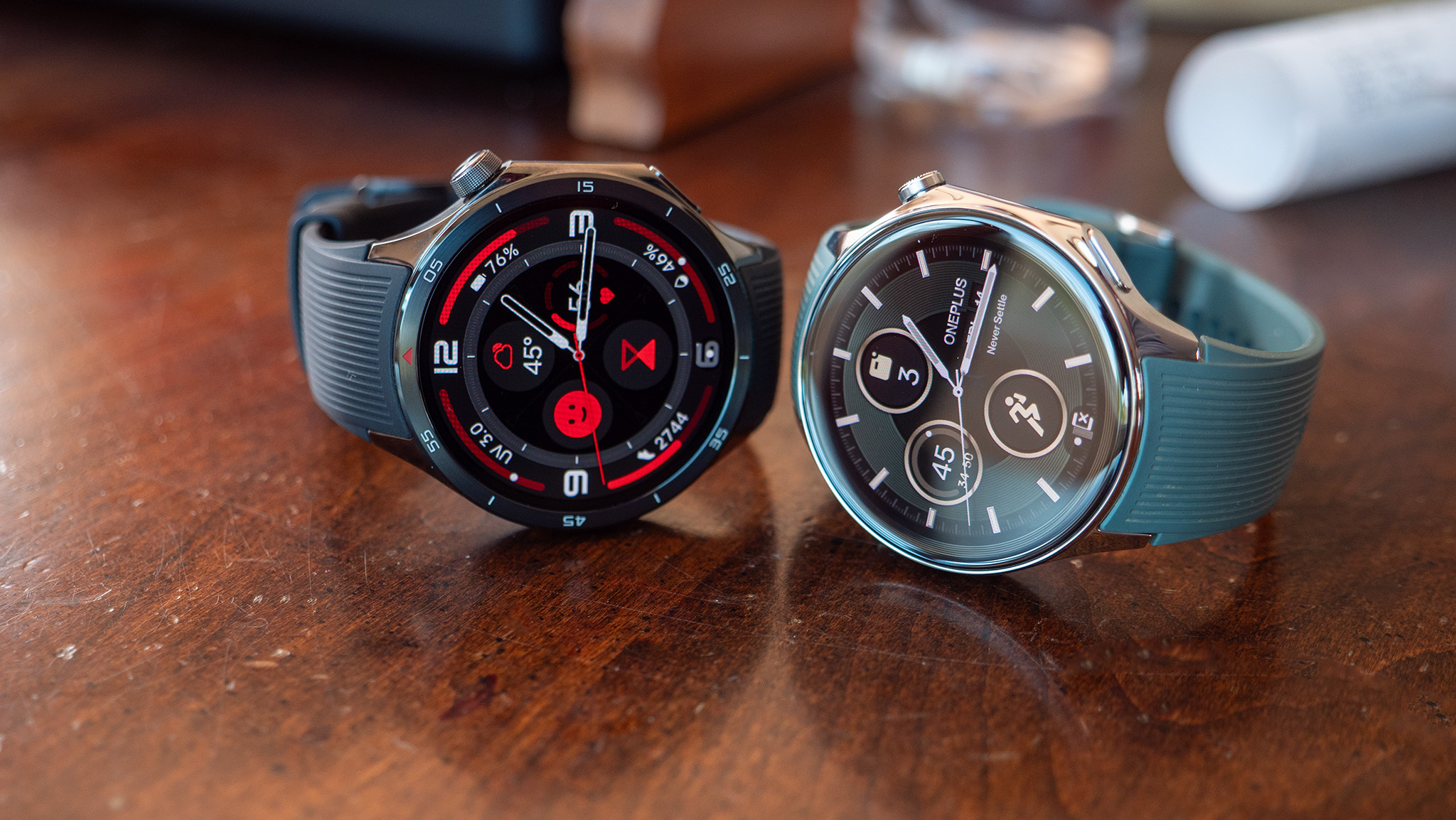 The OnePlus Watch 3 (left) and OnePlus Watch 2 (right) sitting atop a table with their watch faces visible