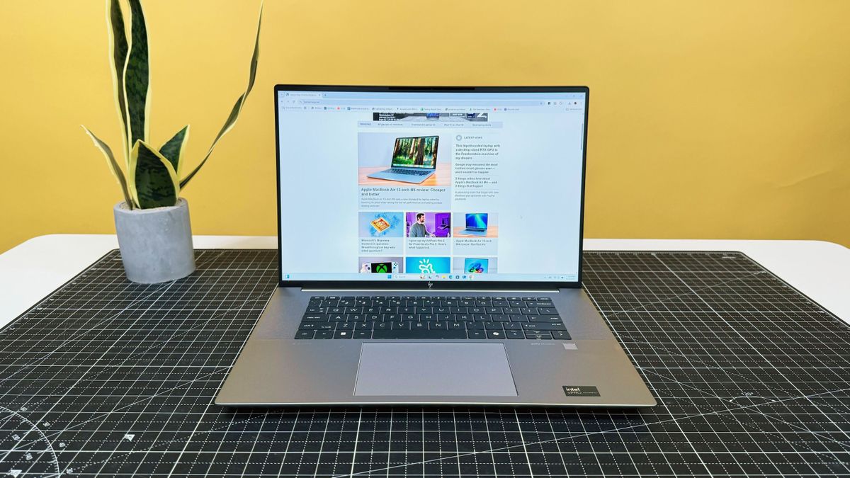 HP ZBook Studio 16 G11 mobile workstation on a white desk with a black table mat, against a yellow backdrop.