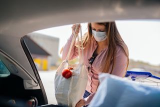 Woman with face mask loading car after shopping while covid-19.