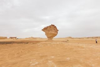 A bg rock in the center of a flat, arid landscape with a grey sky