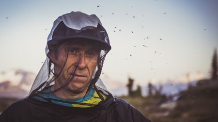 A photo of a man wearing netting surrounded by flies