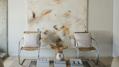 Two modern chairs behind coffee table with contemporary art with flecks of earthy colors mounted on the wall