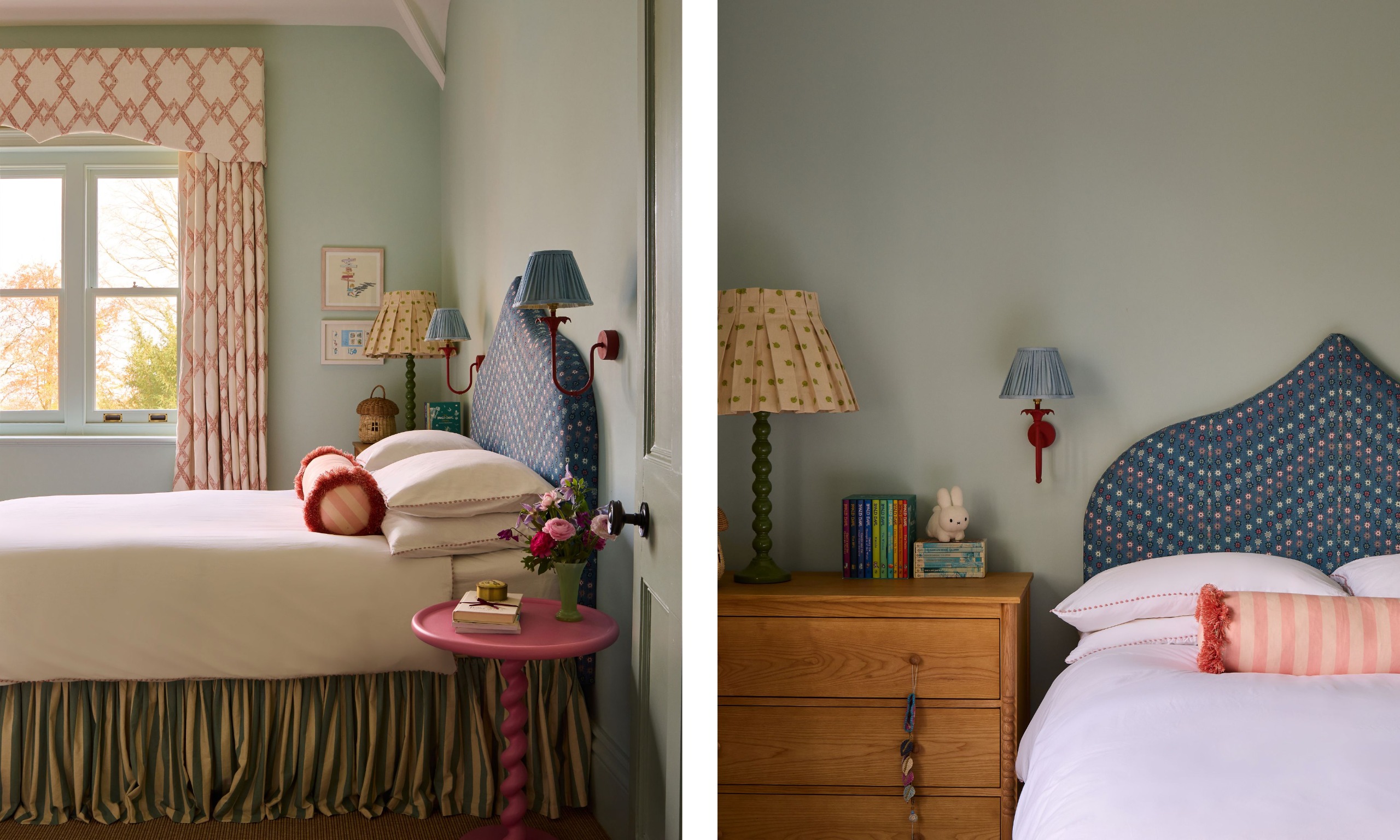 A kid's bedroom with pale blue-gray walls, a dark blue patterned headboard, a striped valance, cream and red curtains, a wood dresser and blue and red wall lights.