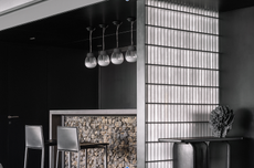 A home bar with black-painted walls, pendant lights above counter, and tall counter chairs, plus a light panel