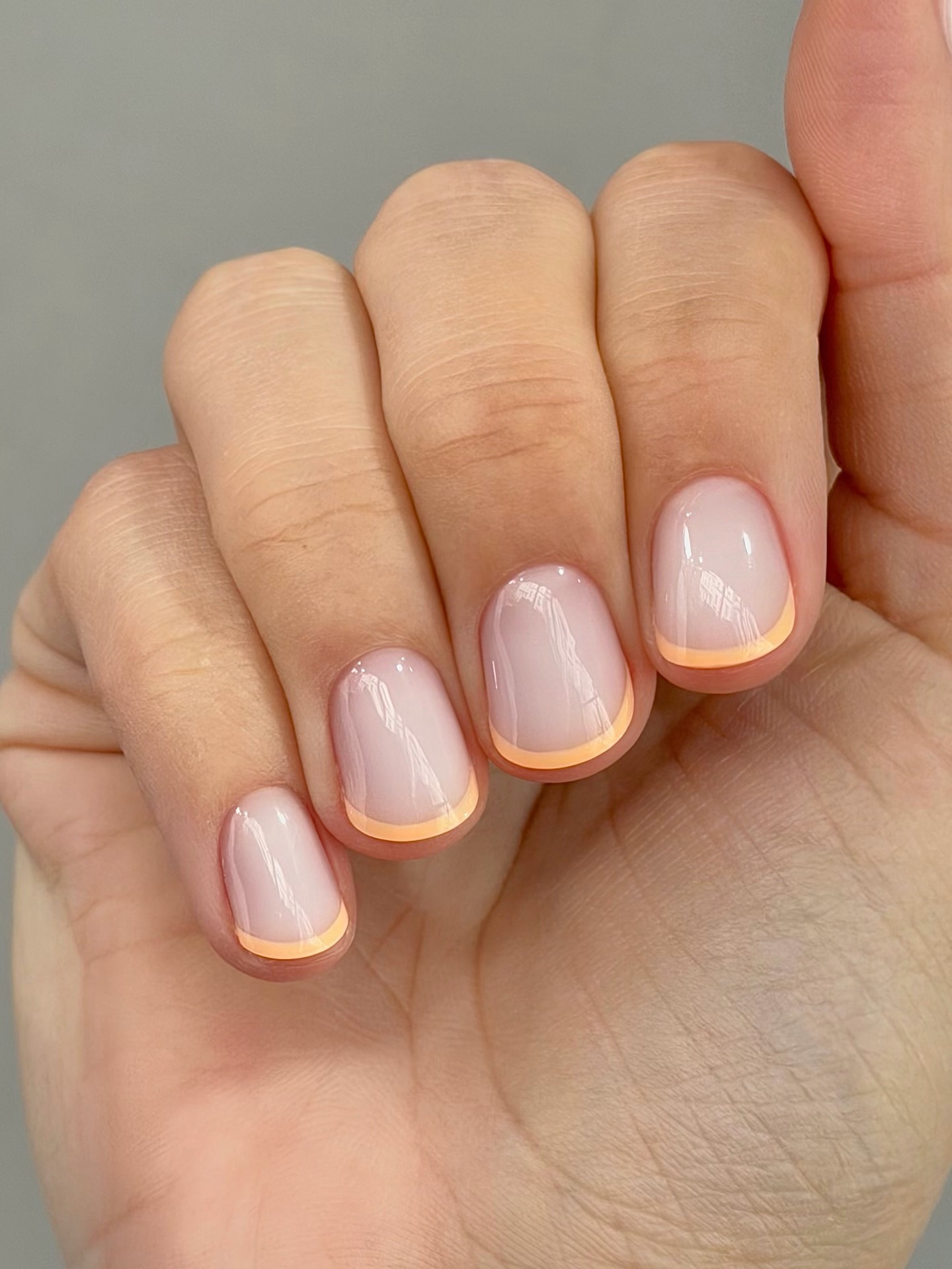 A close-up of a French manicure with pastel peach French tips