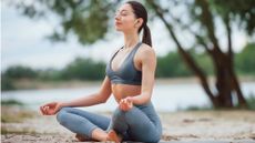 A young woman in a yoga pose listening to EarFun Air Pro 4+ earbuds on a lake or riverside