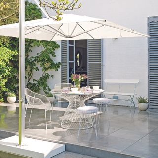 White outdoor table and chairs set with matching white parasol in garden.