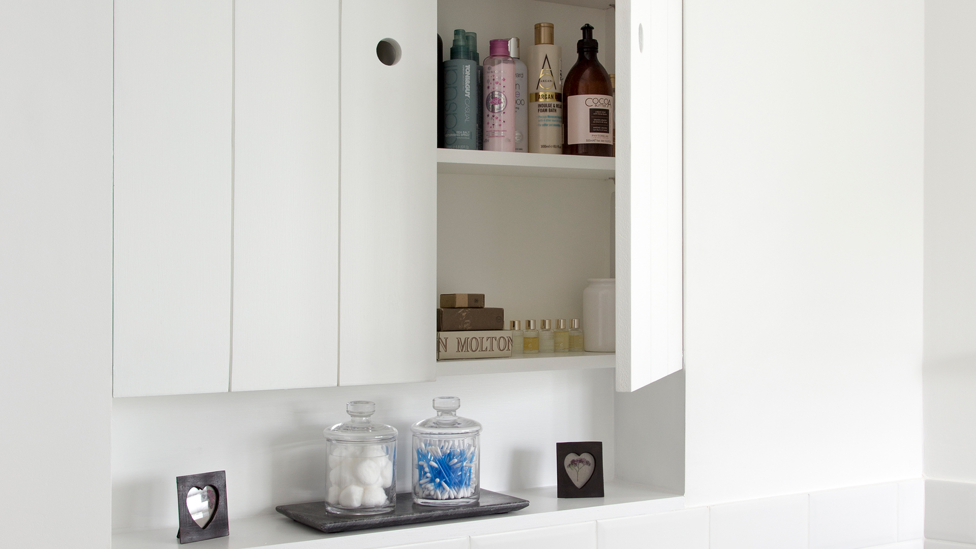White bathroom with a white wall cabinet open to show products inside