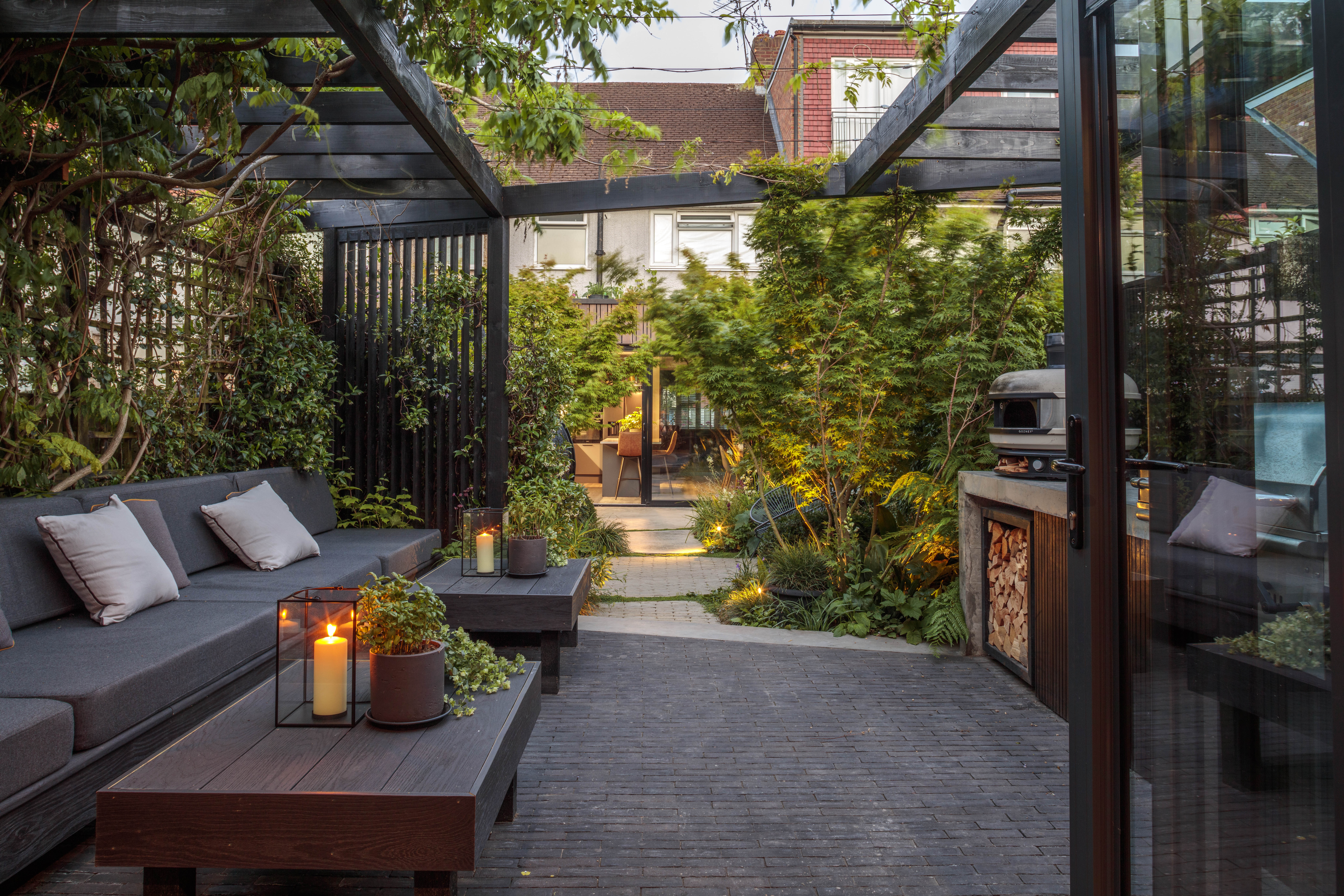 garden outdoor kitchen with tiled patio flooring an outdoor sofa, and lots of leafy greenery