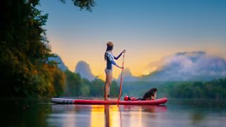 woman paddleboarding in beautiful scenery with her dog