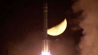 rocket launches with the partially lit moon in the background