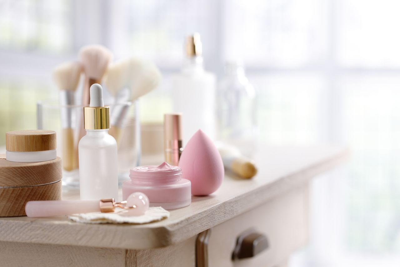 A wooden makeup table with a variety of pink makeup products and serums.