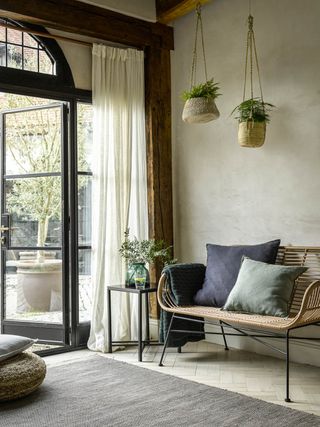 A foyer with large windows, wicker hanging baskets and wicker furniture
