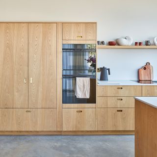 A contemporary, Scandi-style kitchen with pale wooden kitchen cabinets and double ovens