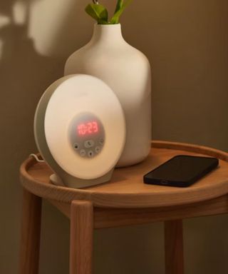 Lumie Bodyclock on a wooden nightstand beside a vase.