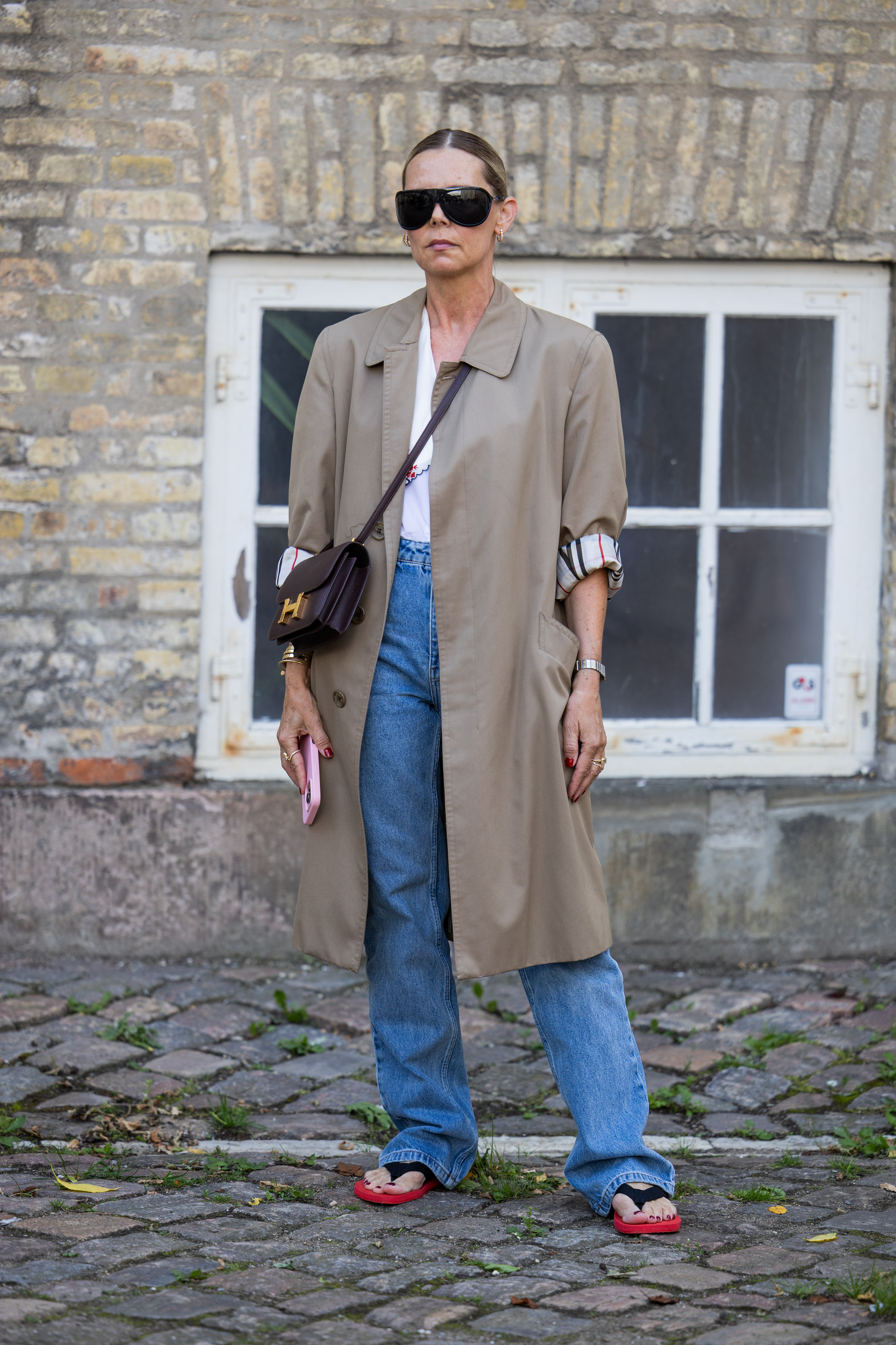 a guest at copenhagen fashion week wears a trench coat with dune flip flops