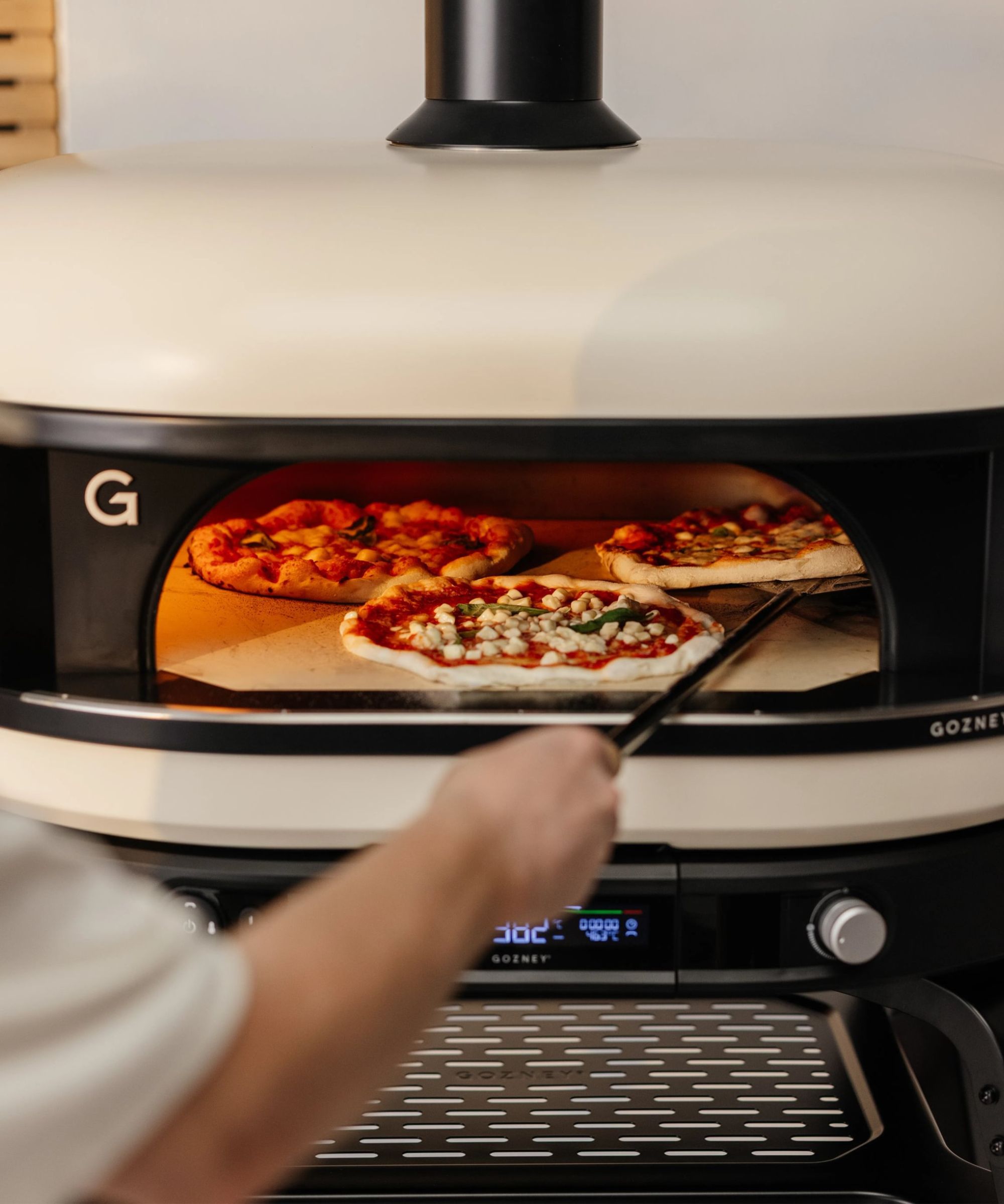 Chef cooking three pizzas in a cream pizza oven