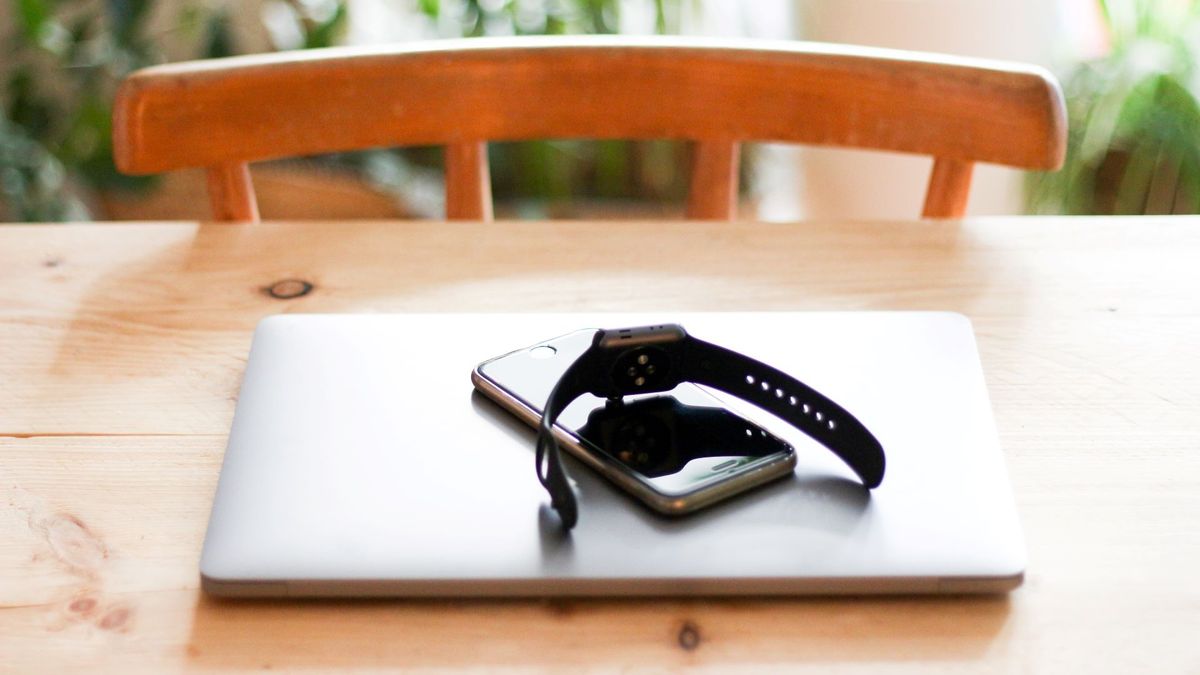 A smart watch, a smart phone and a laptop in a pile on a wooden desk