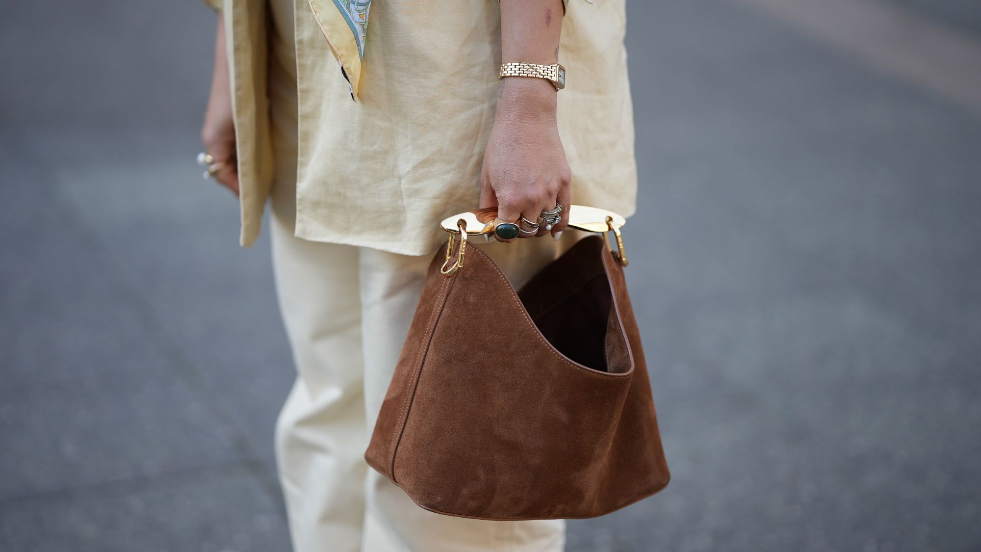 street style shot of woman wearing lots of rings and brown suede handbag