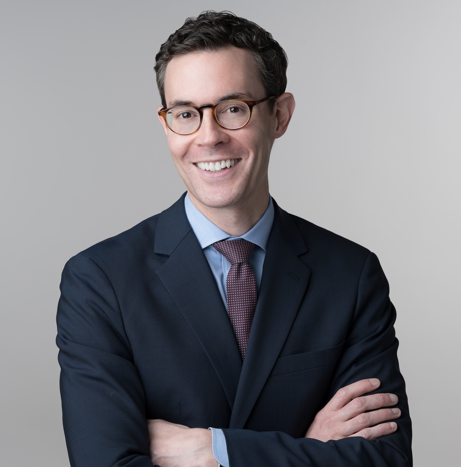 a white man with brown hair and glasses in a navy suit and red tie