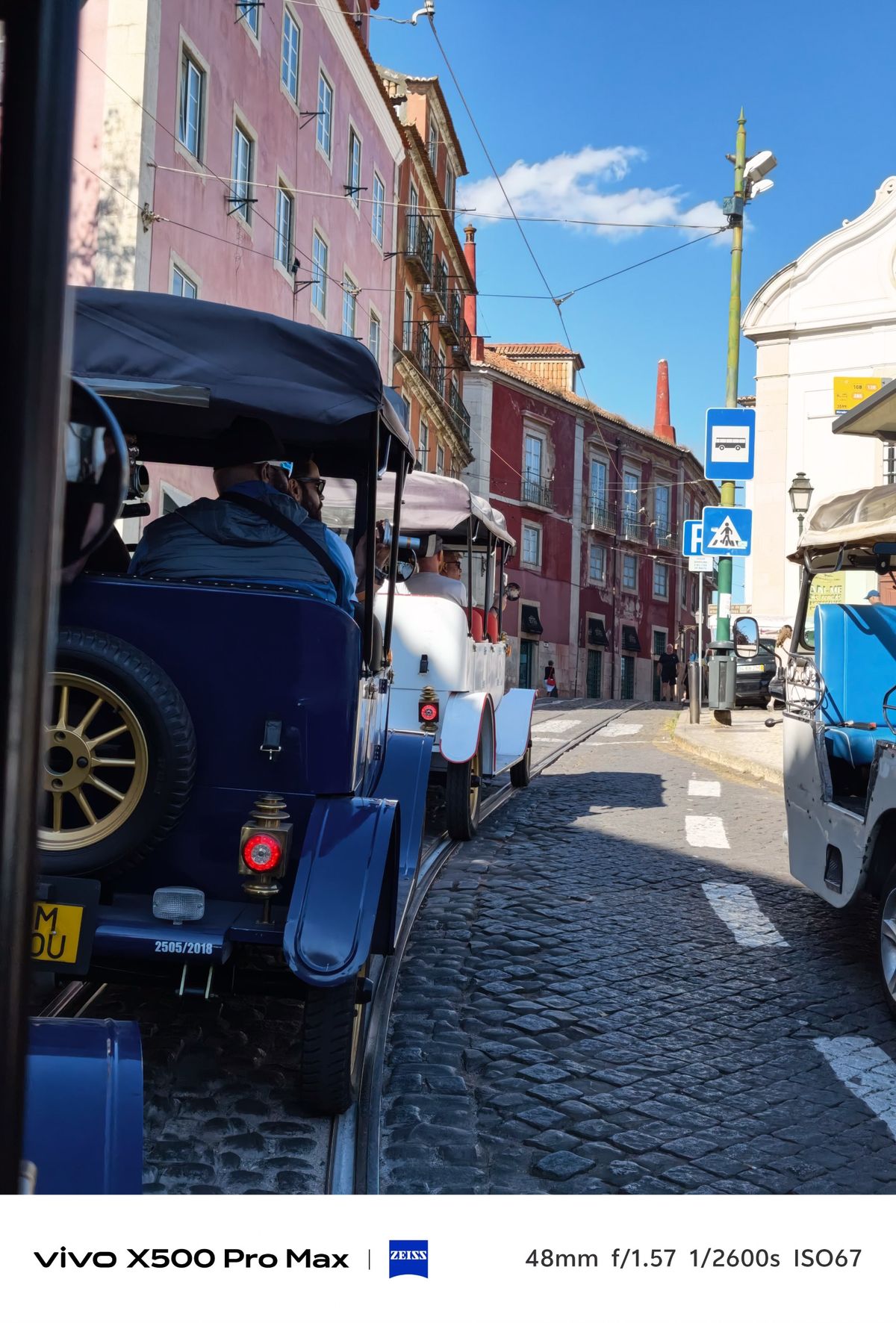 Line of tuk-tuks traveling along a cobbled Lisbon street bordered by colorful historic buildings.