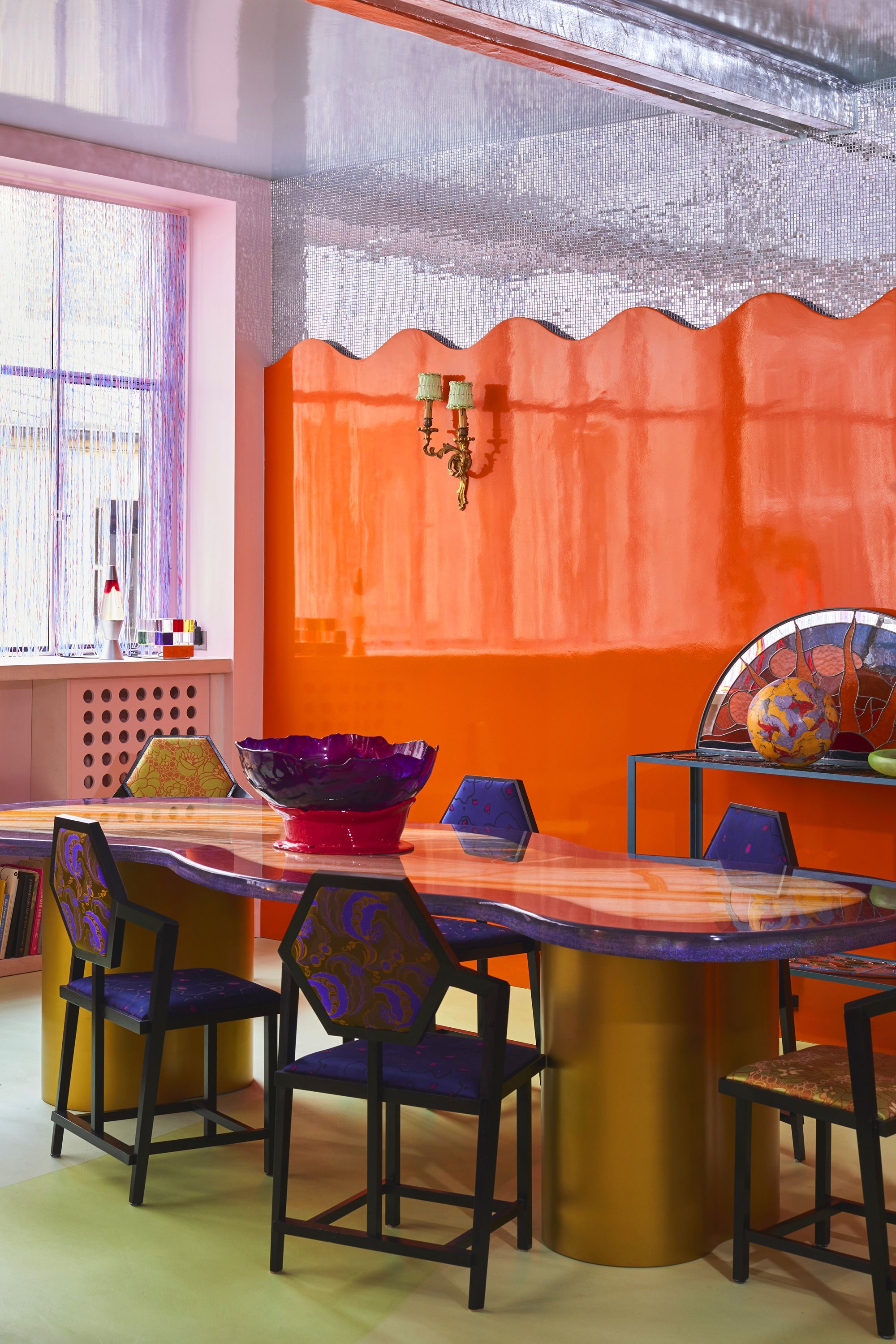a dining room with a purple table, wavy orange wall and silver glitter ball wall
