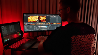 Man using a laptop to edit videos in a darkened home office