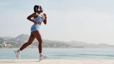 Side view of a young black female athlete running on a stone wall with the coast in the background. Concept of sport and African American ethnicity.