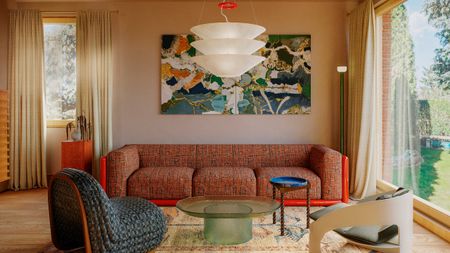 Living room with plaster walls, red sofa, blue armchair and green glass coffee table