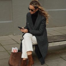 Anouk wears brown suede boots, white jeans, and a gray long coat, and a brown suede jacket.