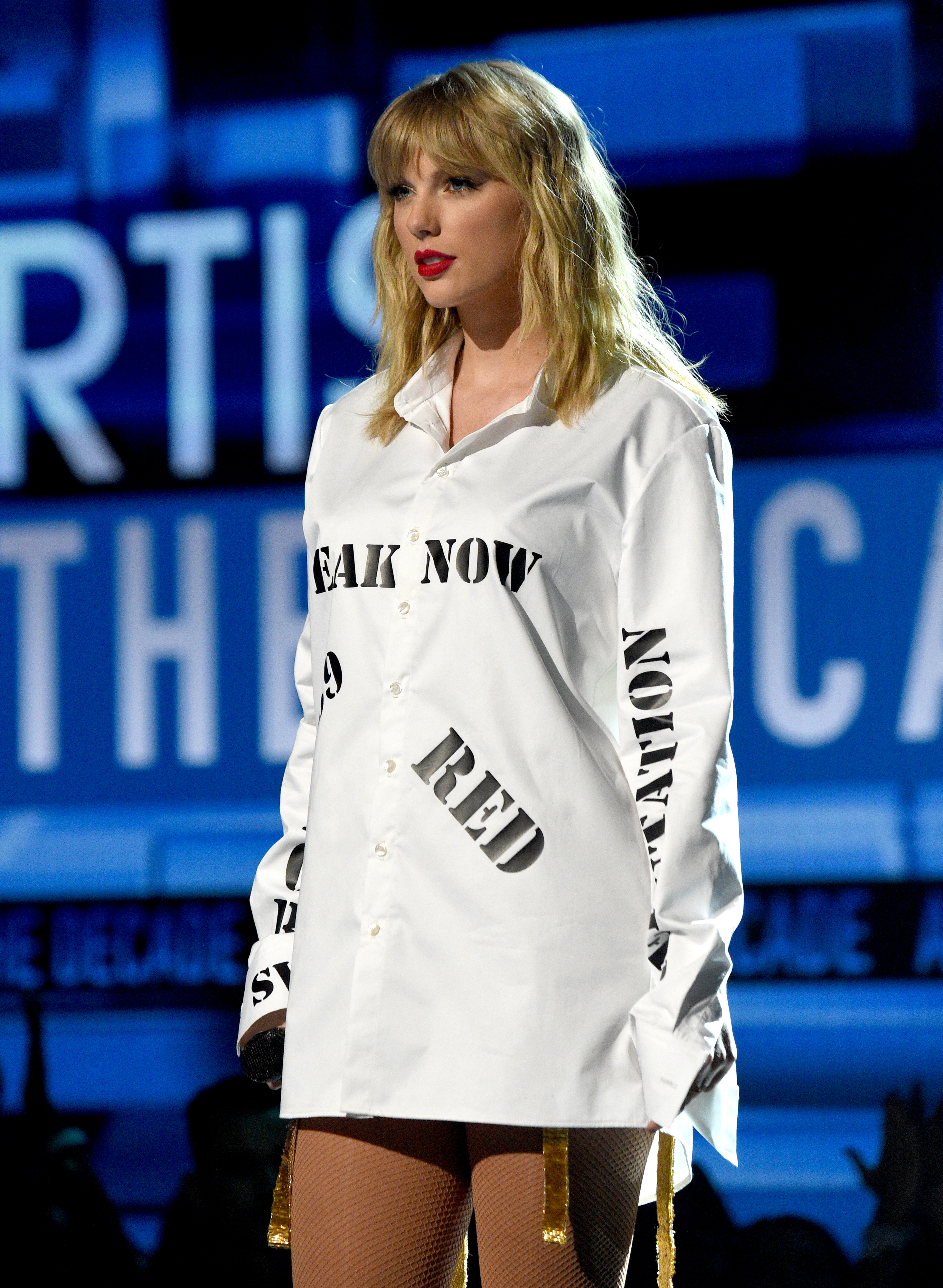 taylor swift performing in a shirt with all her albums printed on it
