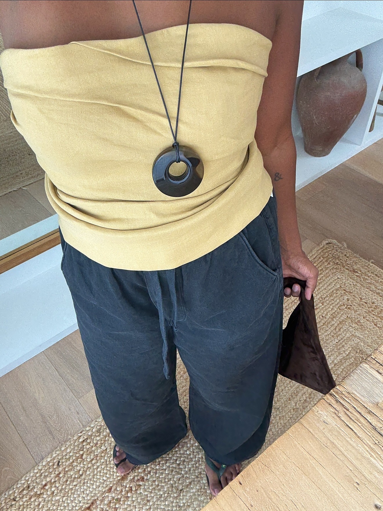 Woman wearing yellow linen top, black linen pants, and black circular stone pendant necklace.