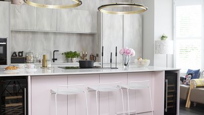 Kitchen with concrete-effect wall units, light pink island, white metal bar stools, dark wood floor, monochrome geometric rug and statement circular pendant lights