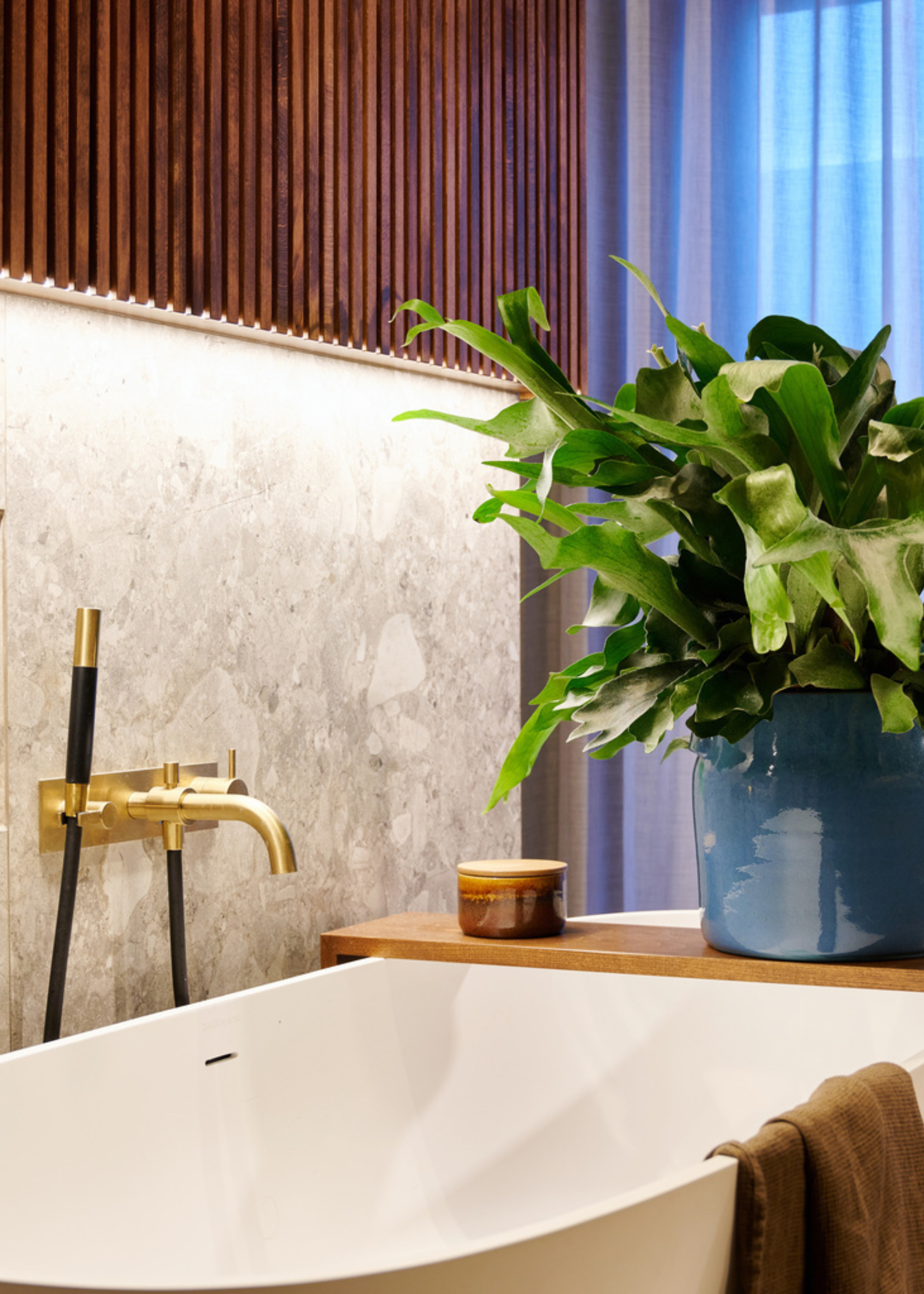 A bathroom with a stone wall, a wood panel wall and a bathtub with a potted plant