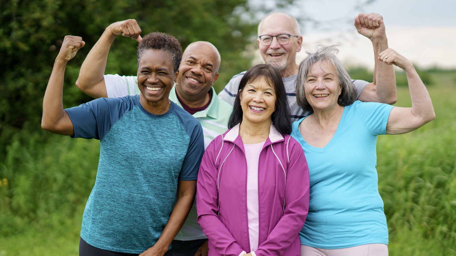 Diverse group of active senior friends in a natural setting, enjoying fitness and camaraderie, demonstrating strength and happiness while celebrating teamwork and healthy living in an outdoor environment.