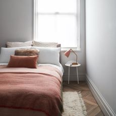 A serene bedroom painted off-white with white bed linen and terracotta-coloured soft furnishings on the bed 