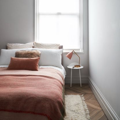 A serene bedroom painted off-white with white bed linen and terracotta-coloured soft furnishings on the bed 