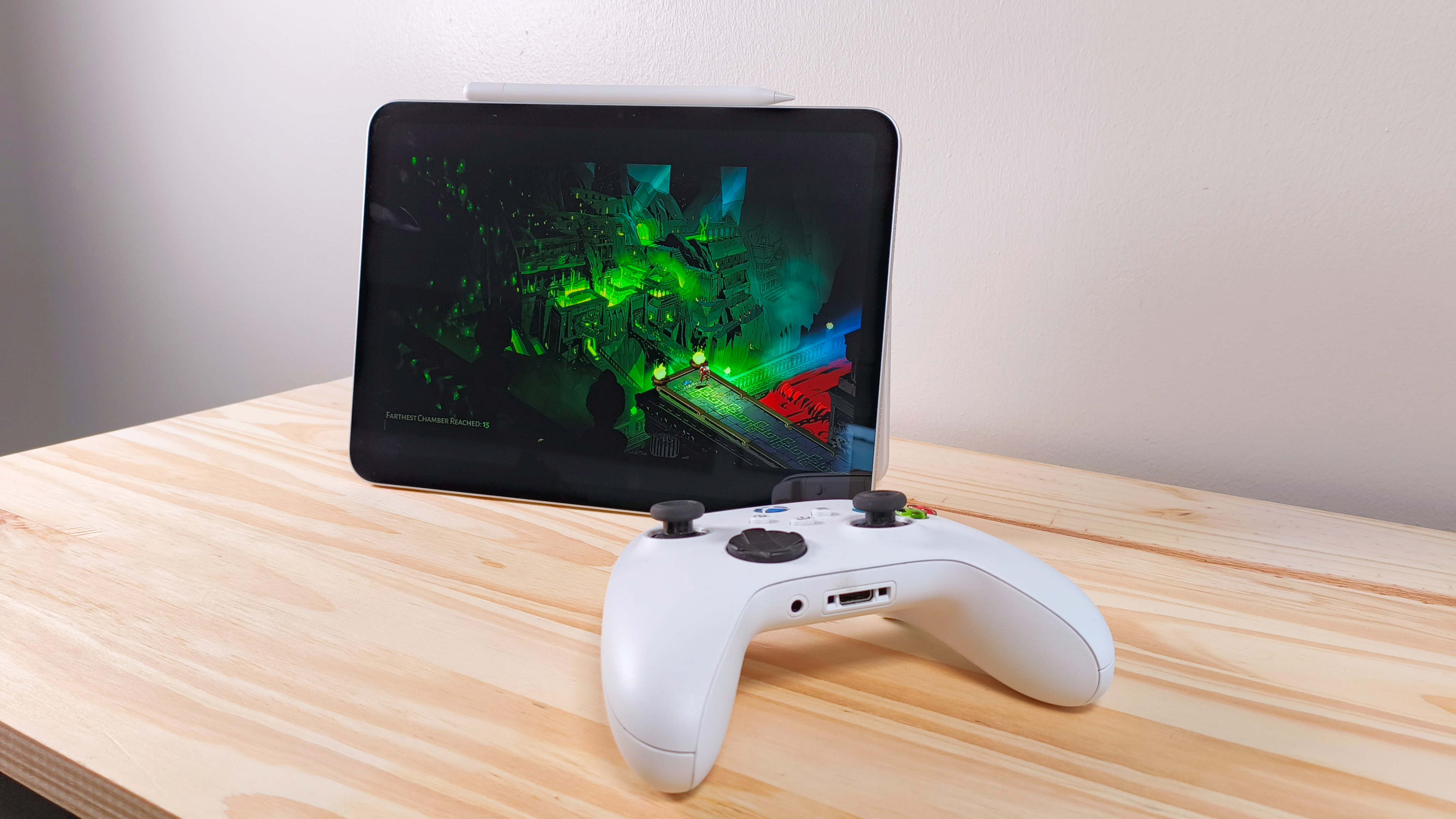 The iPad 11 propped up on a wood table running Hades beside an Xbox controller