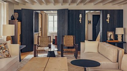 a rustic living room in a french home with ceiling beams, neutral sofas and navy woodwork