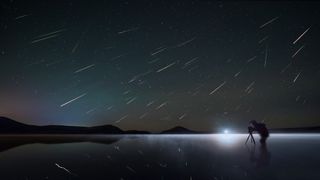 Perseid meteor shower 2024 should be a good display. This image shows a figure looking through a camera lens with perseid meteors raining down from above.