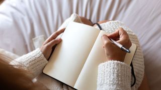 A woman's hands holding a notebook and a pen, about to begin writing in a journal in bed