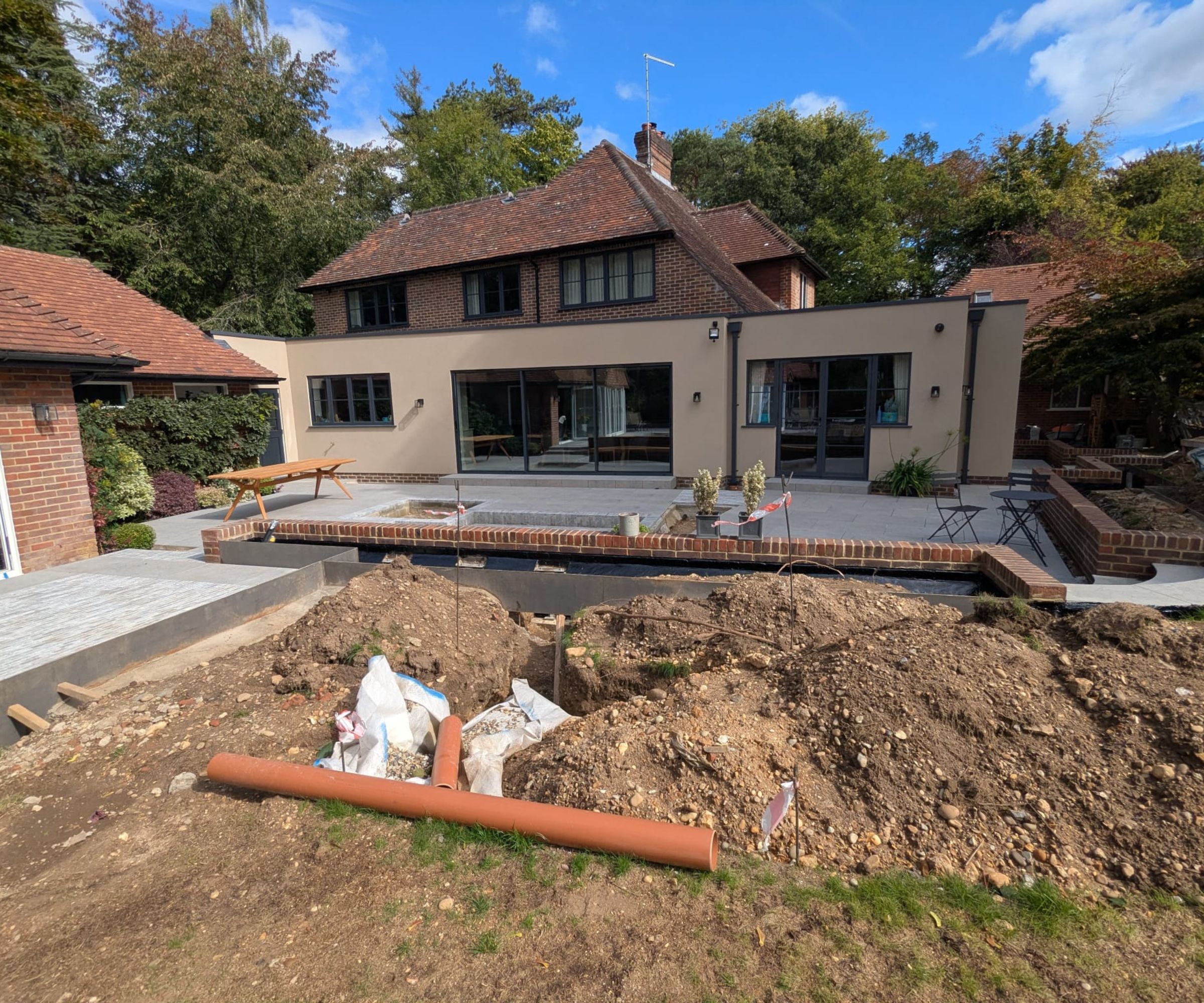 A house transformed with a new rendered single-storey rear extension, large glazed doors opening onto a new stone patio, garden still under construction.