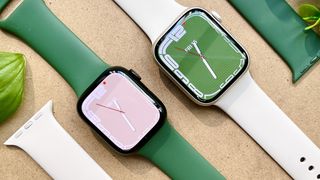 Two green Apple Watch Series 7s lay on a desk top, side by side.