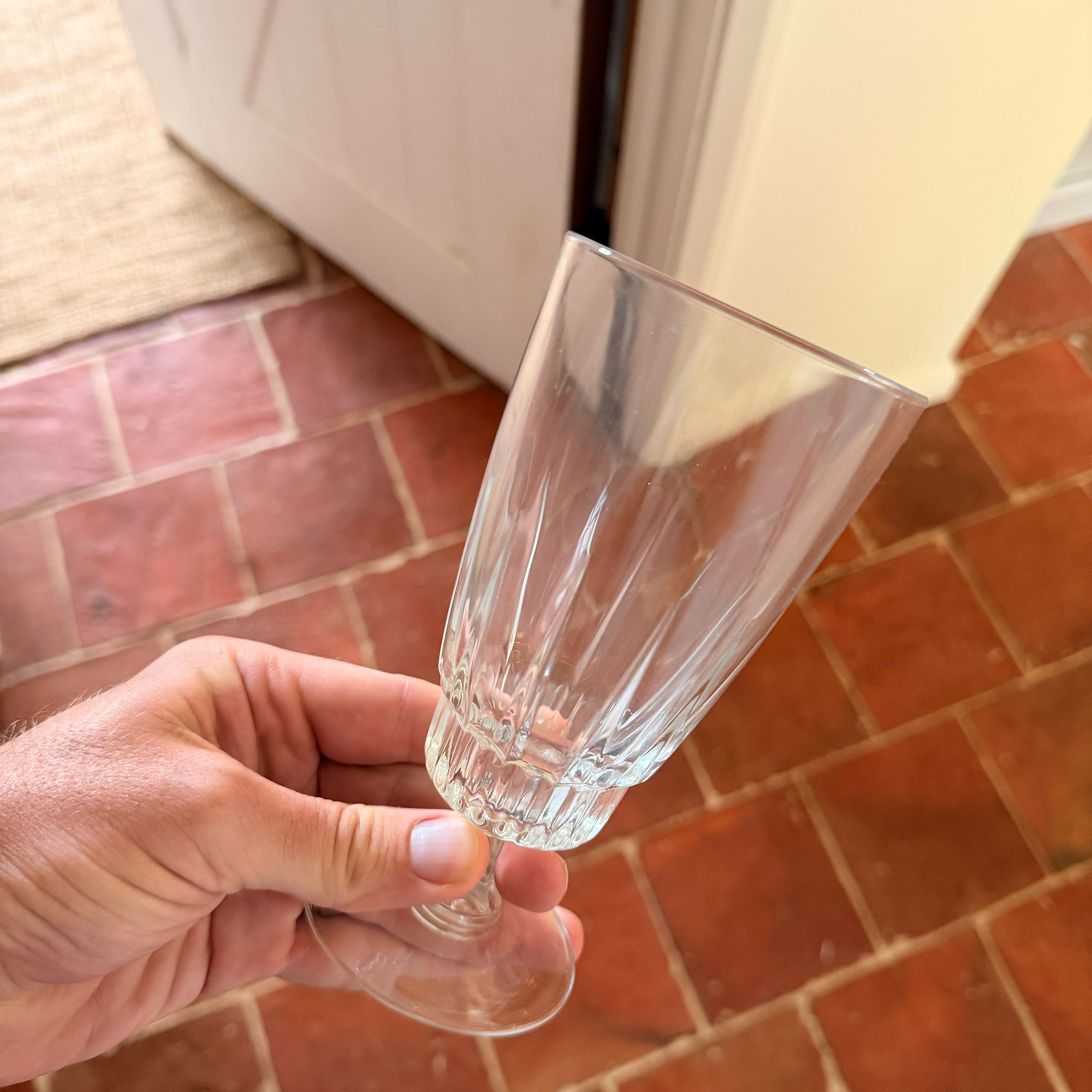 Person holding wine glass above terracotta tiled floor