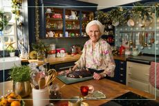 Mary Berry stood next to a Yule Log in a kitchen covered in fairy lights