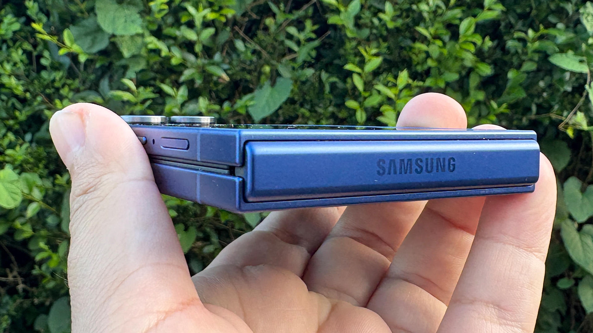 Samsung Galaxy Z Flip 7 smartphone held in hand in garden showing phone's thickness and Samsung logo
