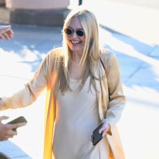 Dakota Fanning wearing a slip maxi dress with heeled white flip-flops and a long-line satin jacket.