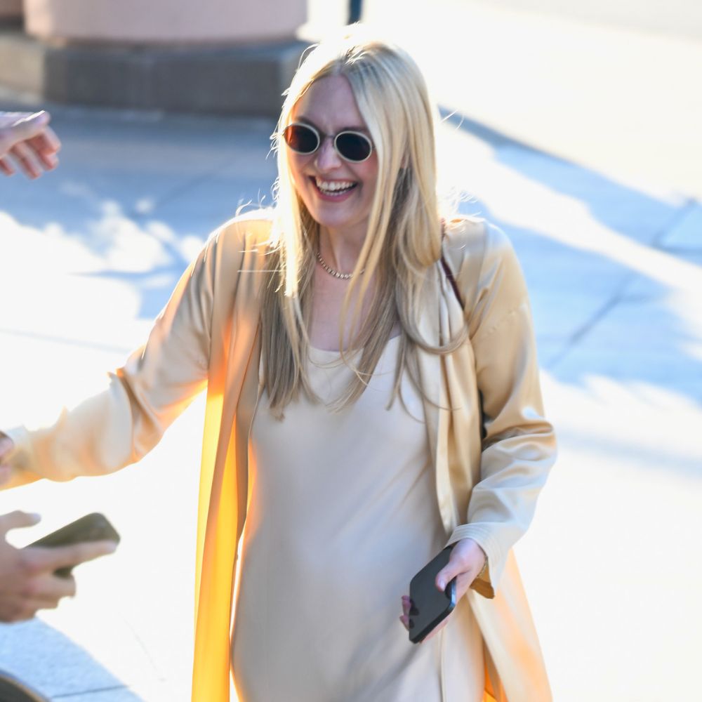 Dakota Fanning wearing a slip maxi dress with heeled white flip-flops and a long-line satin jacket.